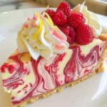 A slice of Heavenly Raspberry Marble Cheesecake topped with fresh raspberries and whipped cream