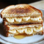 A golden Honey Banana Grilled Cheese Sandwich cut in half, oozing melted cheese and drizzled with honey.